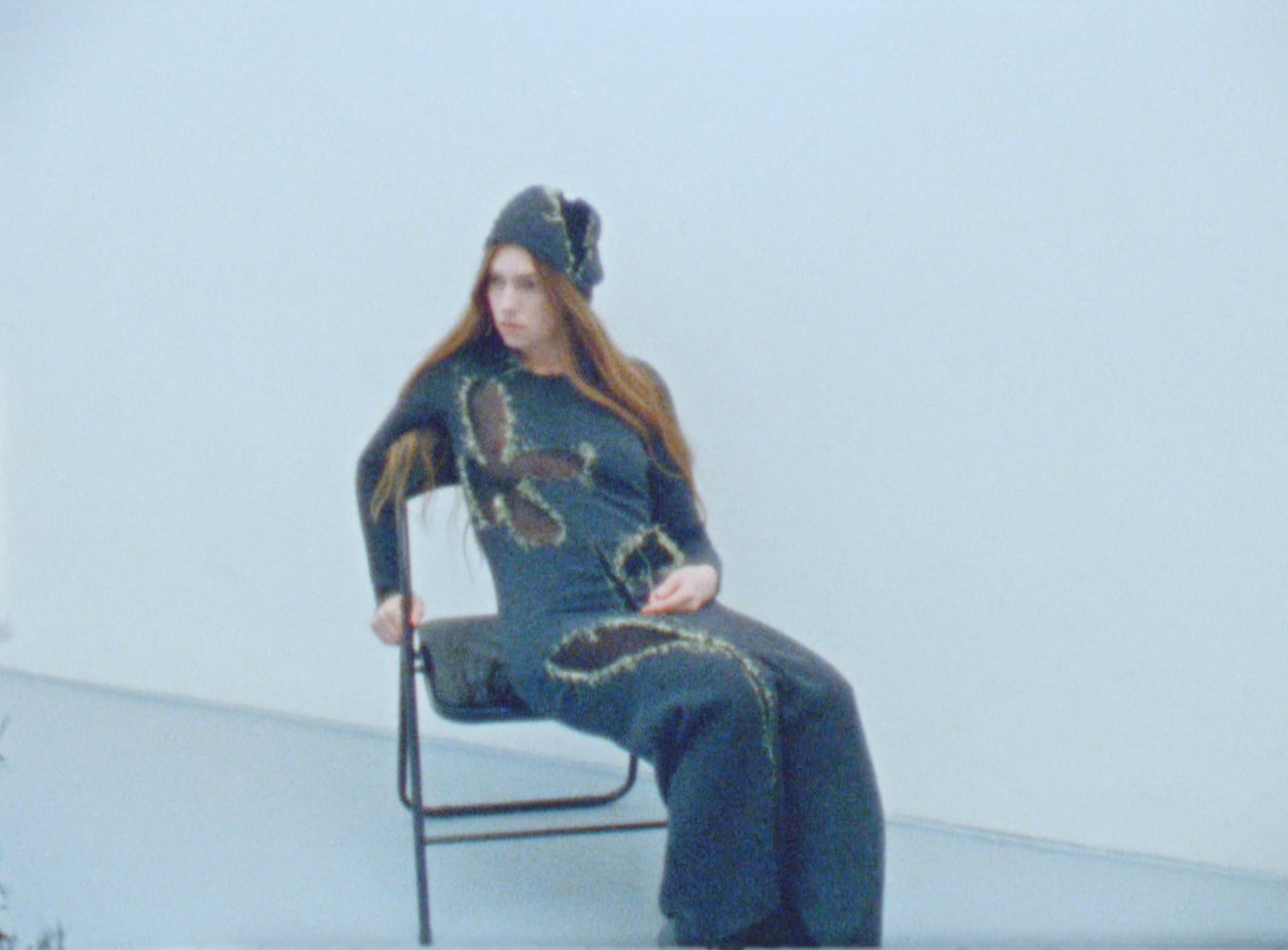femme-assise-chaise-pliante-tenue-robe-verte-foncée-trou-fil debordant-forme-fleur