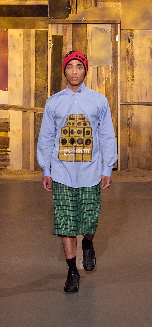homme-tenue-bonnet-rouge-JAH-chemise-bleue-haut-parleur-empile-marron-short-long-ecossais-vert