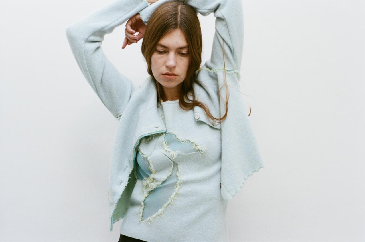 femme-avant-bras-au-dessus-tete-tenue-veste-bleu-clair-trou-forme-fleur-fil-debordant